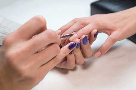 Manicurist removing cuticle with metal pusher on clients girl ring finger. Hand on the black professional pillow. Beauty treatment concept.の写真素材