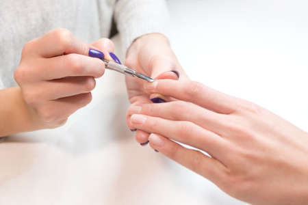 Closeup manicure process with professional tools on female client hand at beauty nail salon. Manicurist gently manicured service.の写真素材