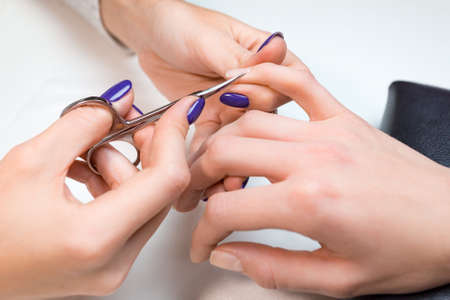 Closeup beautician make the manicure with manicure scissors or nail clippers.Lady having spa treatment on her fingernails from professional manicurist in salon or spa.の写真素材