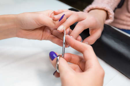 Closeup cuticle clipping, cutting skins manicure treatment with the central finger client in salon nail salon or spa. Hand on the black professional pillow.の写真素材