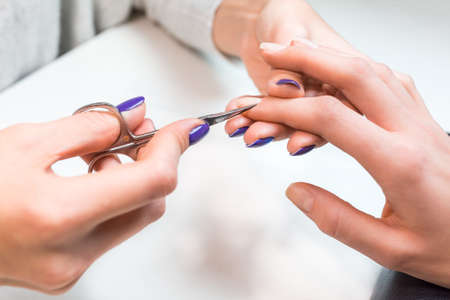 Closeup of manicure applying, cutting the cuticle with scissors. Woman in nail salon receiving manicure by professional beautician.の写真素材