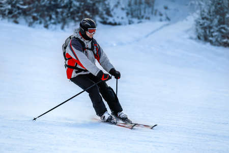 Male skier in red ski suit and mask slides down from the snow slope. Skier skiing downhill in high mountains against sunshine.の写真素材