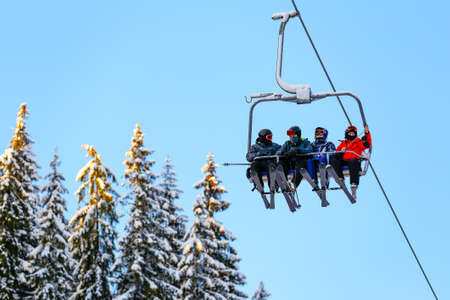 Bottom view of ski family on chair lift in vacation in the mountains. Father, mother and two children with skis and ski gear.の写真素材