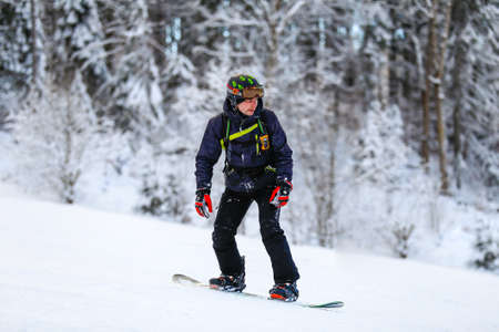 Male snowboarder in black suit and mask slides down from the snow slope. Skier skiing downhill in high mountains against sunshine.の写真素材