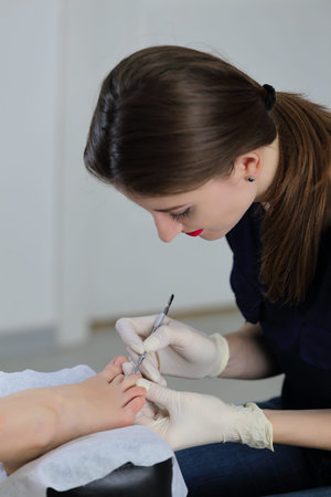 Beautiful manicurist doing service in salon. Specialist removes the cuticle on fingers the client's feet.の写真素材