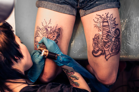 Top view of making tattoo on legs in salon. Showing processing of making a tattoo by woman artist....
