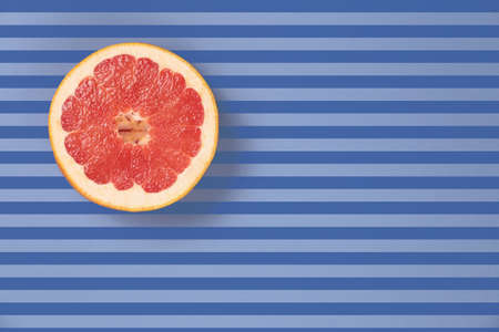 Popart style  red juicy grapefruit on a striped background top view. Striped background in blue and dark blue stripes. Red grapefruit located top left. Lines texture. Diagonal lines.の写真素材