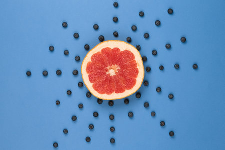 Grapefruit looks like a sun with rays of blueberries on a blue background paper