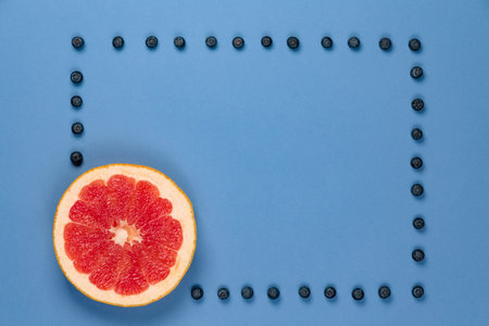 Grapefruit with frame of blueberries on a blue background. It can be used for advertising of healthy...