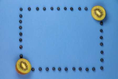 Kiwi with frame of blueberries on a blue background. It can be used for advertising of healthy nutritionの写真素材