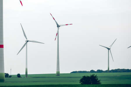 Metal Ecological windmills standing in a green field. Yard of windmill power generator under blue sky. Ecological power with windmill on the field.の写真素材