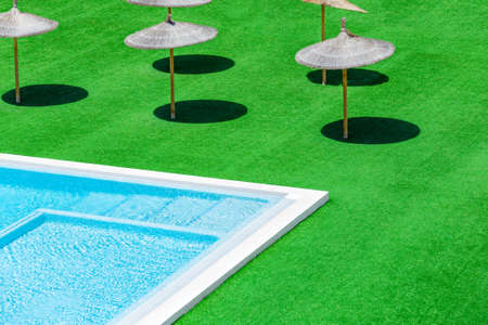 Swimming pool green grass and straw umbrellas with shadow. Sun umbrellas with shadow from the sun. Beach umbrellas near the swimming pool.の写真素材