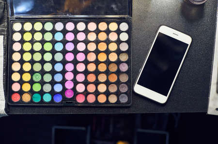 Close up eye shadows palette make up process. Set of professional colorful eyeshadow palette in close-up view with white mobile phone on black table.の写真素材