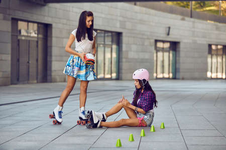 Bruised leg while roller skating girl offer protection for the knees. Scratch on the leg after rollerblading. Two girls sports fun. Active lifestyle.の写真素材