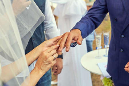 Bride putting a wedding ring on grooms finger. Beautiful place for outside wedding ceremony in wood.の写真素材