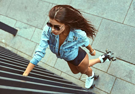 Full length of happy young woman roller skating. Fashion, extreme, youth and people concept - pretty stylish hipster girl rollerblading in the city park, cool roller girl outdoors.の写真素材