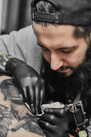 Tattoo master in black gloves, tattoo on the skin of black ink tattoo of his client in the salon.の写真素材