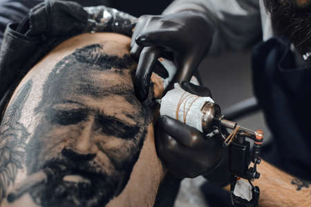 Tattoo master in black gloves, tattoo on the skin the black ink tattoo for his client in the salon.の写真素材