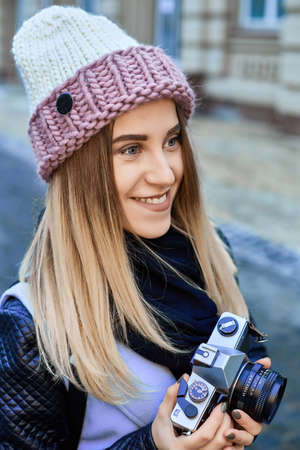 Beautiful girl photographer photographing the old town with retro camera. She is wearing a knitted capの写真素材
