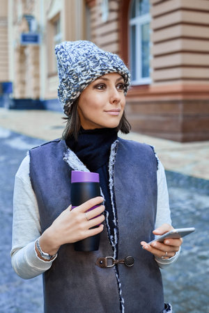 The girl with a smartphone and Thermocup, is walking through the old town
