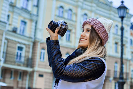 Beautiful girl photographer photographing the old town with retro camera. She is wearing a knitted capの写真素材