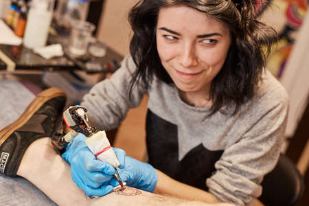Tattoo artist is making tattoo. Master works in a professional salon on a white mat and in sterile blue gloves.の写真素材
