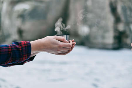 Cup of hot tea in lovers hands against the background of a frozen lake and rocksの写真素材