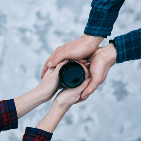 Top view of cup of hot tea in lovers hands against the background of a snowの写真素材