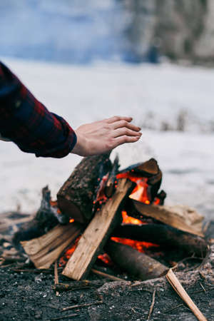 Girl warms hands near a fire in winter. Rocks on backgroundの写真素材