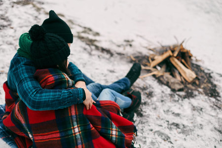 Couple sitting near a bonefire. They are covered with a warm blanket because the is coldの写真素材