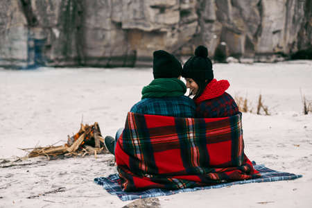 Couple sitting near a bonefire. They are covered with a warm blanket because the is coldの写真素材