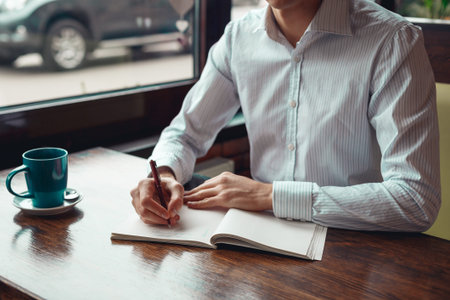 Full concentration man with coffee. Close-up part of young businessman writing in notebook while...