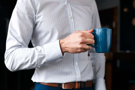 Close up of a businessmans hand with a cup of coffee. A beautiful white shirt and blue pants.の写真素材