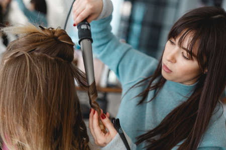 Kyiv, Ukraine - March 3, 2017: Brown haired young woman doing the curling irons in the beauty salon. Close up of stylists hand using curling iron.のeditorial素材