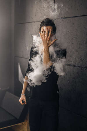 Vaping man holding a mod. A cloud of vapor. Black background. Smoking electronic cigarette Vape advertisement conceptの写真素材