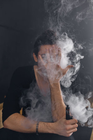 Vaping man holding a mod. A cloud of vapor. Black background. Smoking electronic cigarette Vape...