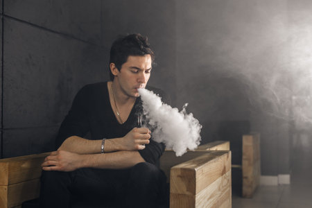 Vaping man holding a mod. A cloud of vapor. Black background. Smoking electronic cigarette Vape...
