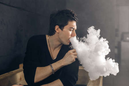 Vaping man holding a mod. A cloud of vapor. Black background. Smoking electronic cigarette Vape advertisement conceptの写真素材