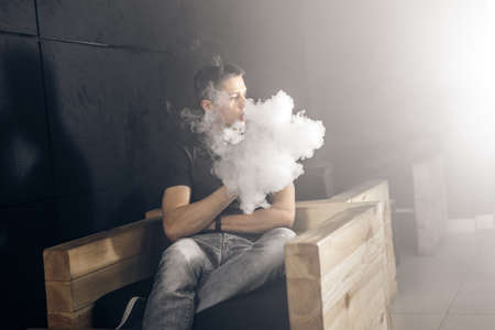Vaping man holding a mod. A cloud of vapor. Black background. Smoking electronic cigarette Vape advertisement conceptの写真素材