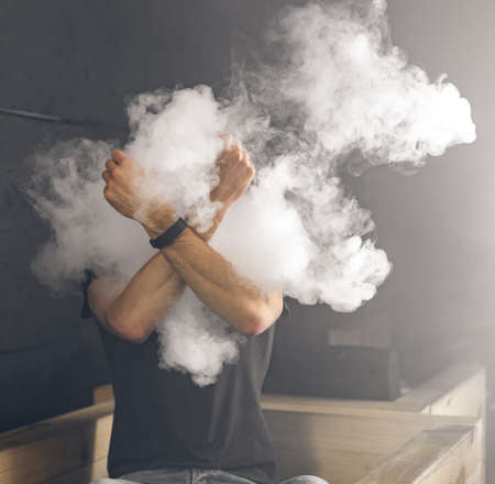Smoke sticks out of the smoke. Man is vaping in the dark roomの写真素材