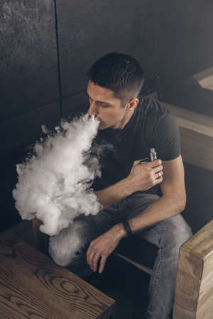 Vaping man holding a mod. A cloud of vapor. Black background. Smoking electronic cigarette Vape advertisement conceptの写真素材