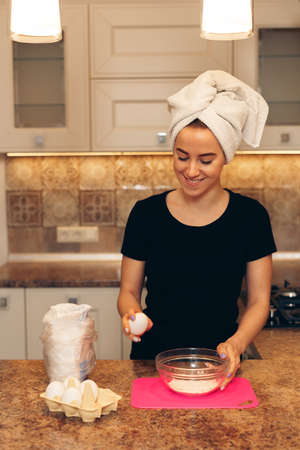 Young woman with a towel on her head makes breakfast. Woman breaks the eggs.の写真素材