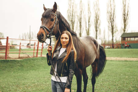 Beautiful girl communicates with the horse in the park. Preparing for the ridingの写真素材