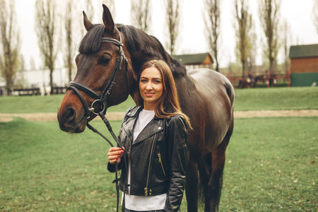 Beautiful girl communicates with the horse in the park. Preparing for the riding