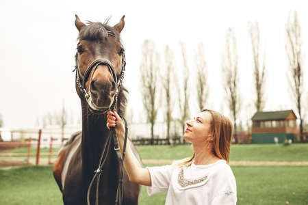 Beautiful girl communicates with the horse in the park. Preparing for the ridingの写真素材