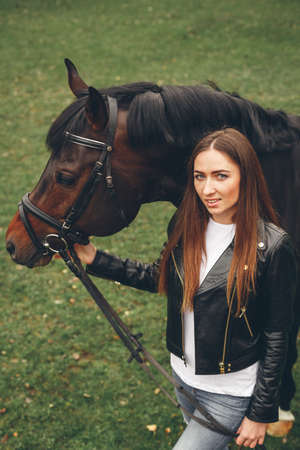 Beautiful girl communicates with the horse in the park. Preparing for the ridingの写真素材