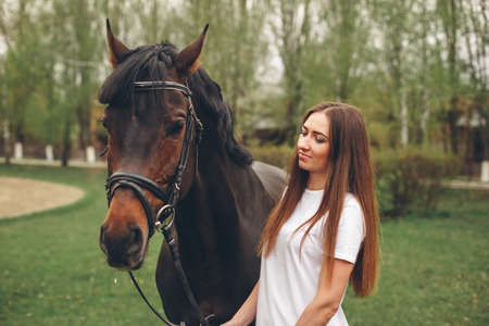 Beautiful girl communicates with the horse in the park. Preparing for the ridingの写真素材