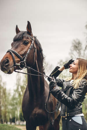 Beautiful girl communicates with the horse in the park. Preparing for the ridingの写真素材