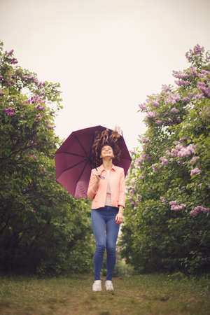 Happy girl with umbrella in park with Lilac that bloomsの写真素材