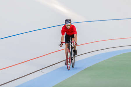 Racing cyclist on velodrome outdoor. Professional athlete in a red T-shirt and a black bicycle.の写真素材